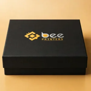 Custom chocolate gift boxes as an elegant rigid gift box in deep matte tones with the Bee Printers logo printed on the lid, closed hero box on a warm golden-beige studio backdrop