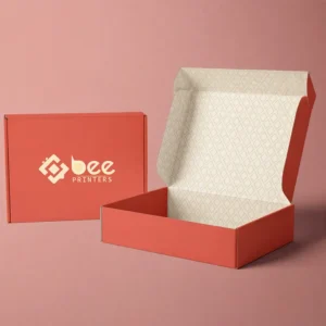 Two coral mailer boxes on a pink background, one closed standing behind with the Bee Printers logo in cream in its centre and one open and empty in front showing a cream diamond-patterned interior, showing custom 6 x 6 x 4 single wall cardboard boxes.