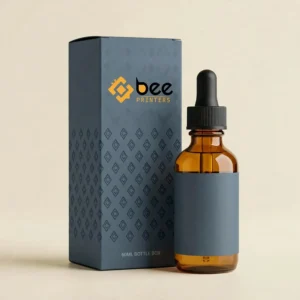 Slate blue closed box with a dark diamond pattern and the Bee Printers logo beside an amber dropper bottle with a matching slate label and black cap on a cream background, showing custom 60ml bottle boxes