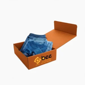 Open orange mailer box filled with folded blue clothing including jeans, a checked shirt and a sweater on a plain white background, showing custom apparel subscription boxes
