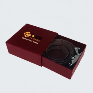 Burgundy slide box partly open to reveal a coiled brown leather belt with a silver buckle on a light grey background, showing custom belt boxes.