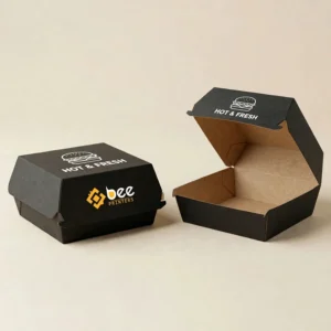 Two black clamshell boxes on a cream background, one closed in front and one open and empty showing its brown interior, both with a white burger icon and HOT & FRESH text on the lid and the Bee Printers logo on the closed box, showing custom black burger boxes.