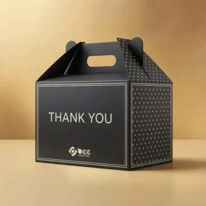 A closed box from the custom black gable boxes range in matte black with white polka dots and THANK YOU text stands on a gold beige background with the Bee Printers logo on the front.