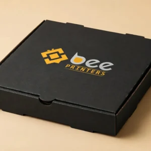 Hero shot of a matte black flat pizza box with the Bee Printers logo printed on the closed lid, warm golden-beige studio backdrop