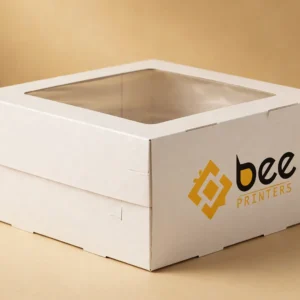 Custom cake box in white board with a clear window lid and the Bee Printers logo printed on the side, closed hero box on a warm golden-beige studio backdrop