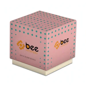 A closed pink cube box patterned with small teal diamonds, sitting on a cream base and printed with the Bee Printers logo and Bath Bomb Boxes wording on two sides, appears on a white background, showing custom cbd bath bomb boxes.