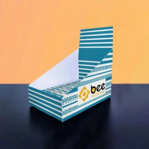 An empty teal and white striped display tray with a plain rectangular header card and circular cut-outs visible in its insert tray, set against an orange wall on a dark surface with the Bee Printers logo on the front, showing custom cbd display boxes wholesale in a neutral geometric print.