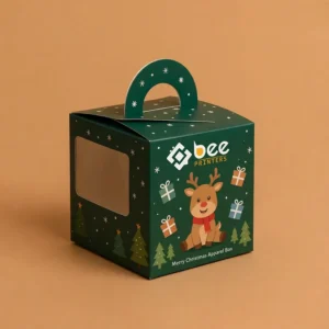 Closed dark green handle box with a side window, reindeer, gift and Christmas tree artwork and the Bee Printers logo on a tan background, showing custom christmas apparel boxes.