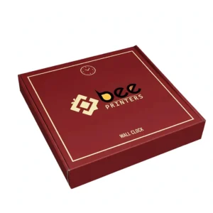 A closed flat burgundy square box with a cream border, a small clock icon and WALL CLOCK text on a white background, showing custom clock boxes packaging