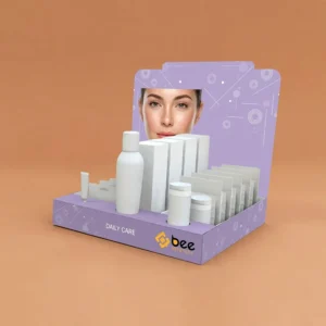 A lilac purple counter display with a woman's face printed on its flat header and Daily Care text on the front tray, holding plain white bottles, boxes, jars and sachets on a warm tan background with the Bee Printers logo, showing custom cosmetic display boxes wholesale.