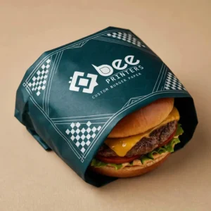 Deep teal burger paper with a white checkerboard pattern and a large white Bee Printers logo wrapped around a cheeseburger with lettuce and tomato on a plain beige background, showing custom custom burger paper