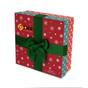 A closed red square decorative box with white snowflakes and stars, a wide dark green ribbon bow, Merry Christmas lettering and the Bee Printers logo on a white background, showing custom decorative christmas boxes.
