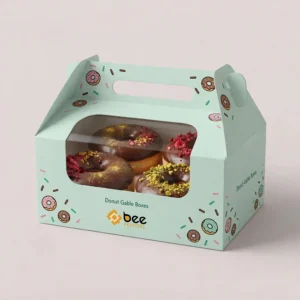 Mint-green custom donut gable boxes with a clear front window showing four chocolate-topped donuts, decorated with small donut and sprinkle illustrations and the Bee Printers logo on a pale pink background.