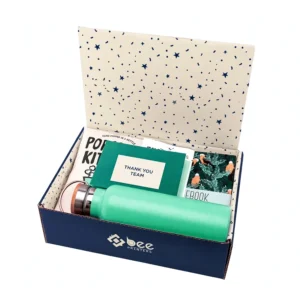 Open navy custom employee appreciation boxes with a cream star-pattern inside lid, filled with a green water bottle, a THANK YOU TEAM card and notebooks on a white background, with the white Bee Printers logo on the front.
