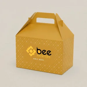 A mustard-yellow custom gable boxes 9x6x6 design with a small white dot and diamond pattern, a die-cut carry handle and the Bee Printers logo on the front, on a cream background.