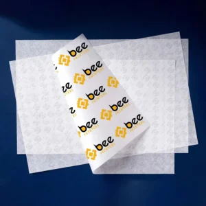 Overlapping flat white greaseproof paper sheets on a dark blue background, with the folded centre sheet printed with a large bold repeating Bee Printers logo in yellow and black, showing custom greaseproof paper.