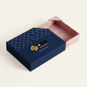 A navy blue card holder box with a white diamond grid pattern and the Bee Printers logo on its lid, partly open to reveal an empty pink tray, on a plain off-white background, showing custom leather card holder boxes.