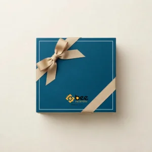A closed teal square gift box with a beige ribbon bow and a white border line with the Bee Printers logo at the bottom centre viewed from above on a cream background, showing custom luxury gift boxes.