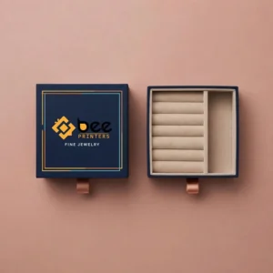 A navy blue jewellery box viewed from above with its closed lid on the left and its open beige ring-roll interior on the right with the Bee Printers logo on the lid on a dusty pink background, showing custom luxury jewelry boxes.