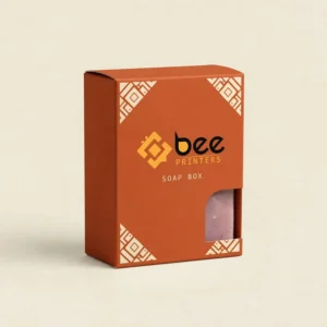 A burnt orange soap box with cream geometric corner patterns standing closed with a die-cut window showing pink soap inside on a cream background, showing custom luxury soap packaging boxes