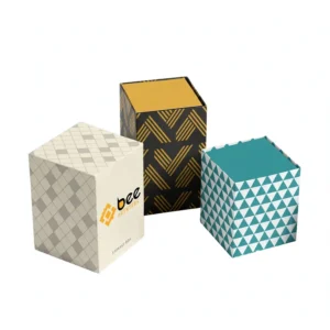Three closed cube storage boxes in cream diamond, black and gold stripe, and teal triangle patterns with Bee Printers logo on one box on a white background, showing custom marijuana packaging