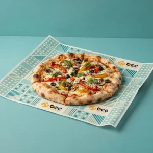 A whole vegetable pizza with peppers, olives and basil served on a flat square liner printed in teal and cream geometric dots, squares and stripes on a teal background, showing custom pizza liners