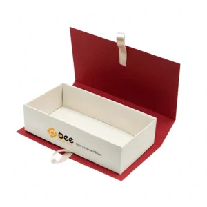 Open white rectangular rigid tray inside a red hinged book-style cover with cream ribbon loops on a white background, showing custom rigid cardboard boxes