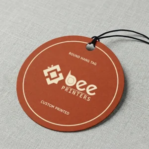A single terracotta-brown custom round hang tags with cream Bee Printers logo, thin cream border and black string on a light grey fabric background.