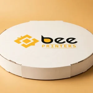 Custom round pizza box in warm white with the Bee Printers logo printed on the closed round lid, single hero box on a warm golden-beige studio backdrop