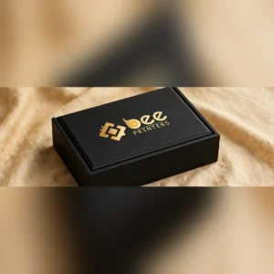 Custom shoulder neck rigid boxes in matte black with the gold Bee Printers logo on the lid against a warm beige linen backdrop