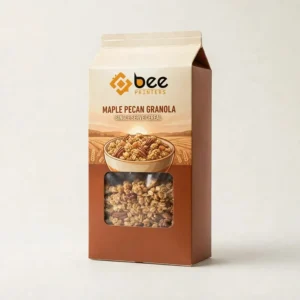 Brown and cream gable-top Maple Pecan Granola single serve cereal box with the Bee Printers logo at the top, a bowl of granola over a wheat field illustration and a rectangular window showing granola with pecans on an off-white background, showing individual cereal boxes