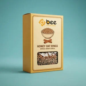 Mustard yellow Honey Oat Rings whole grain cereal box with a cream front panel, the Bee Printers logo at the top, a bowl and cinnamon sticks illustration and a rectangular window showing oat ring cereal on a teal background, showing yellow cereal boxes